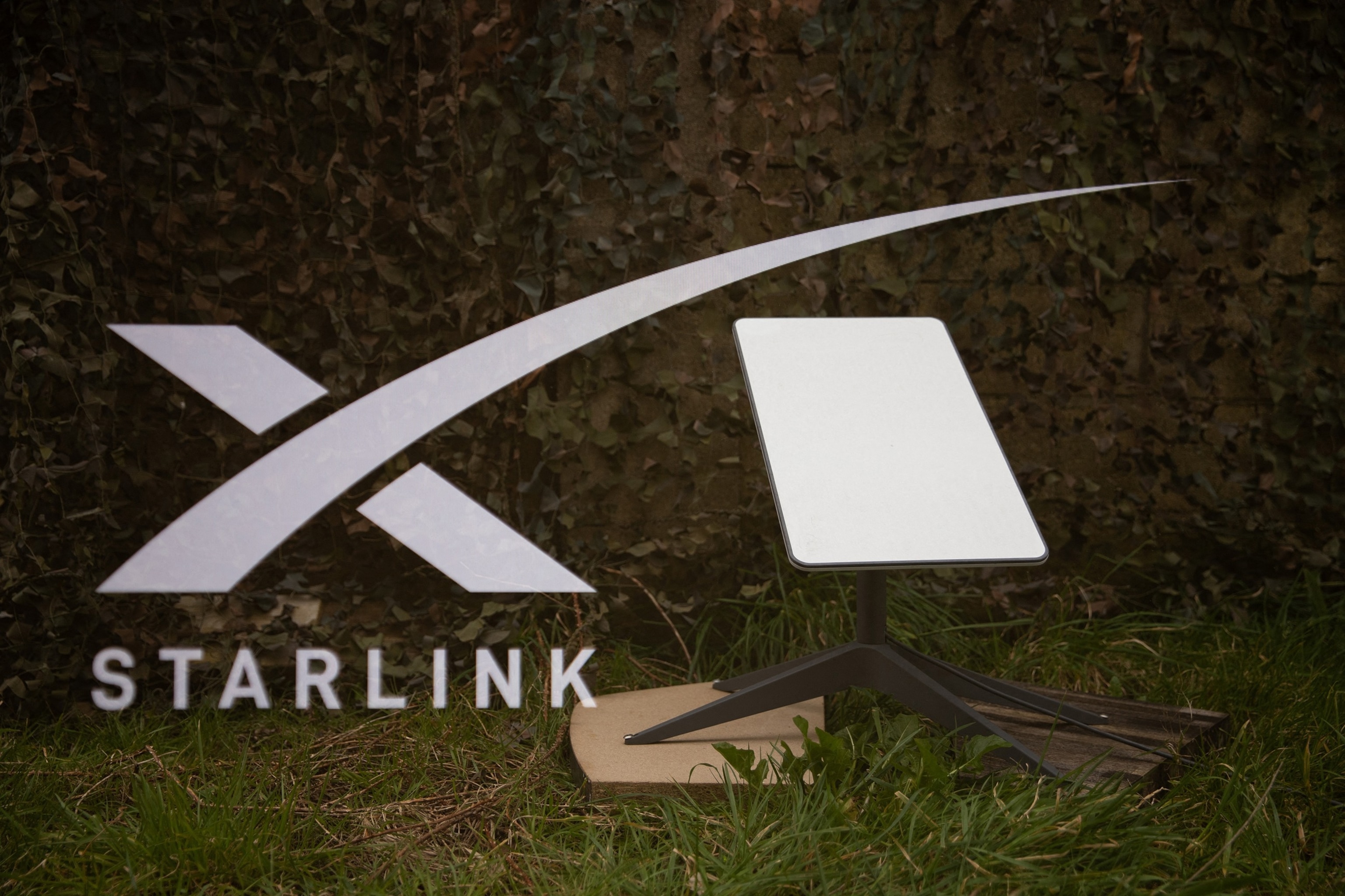 In this March 1, 2025, flie photo, a double exposure photograph shows the starlink logo and satellite antenna on the ground in front of a military camouflage net in Kerlouan in Brittany in France.Vincent Feuray/Hans Lucas/AFP via Getty Images