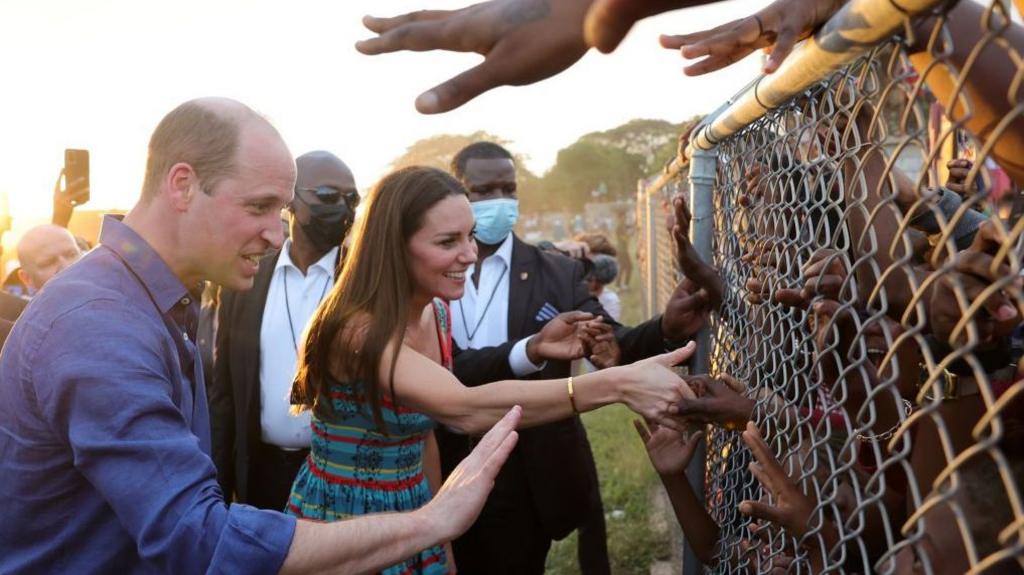 Image caption,The Duke and Duchess of Cambridge shook hands with children through a wire fence during a visit to Trench Town on their 2022 tour