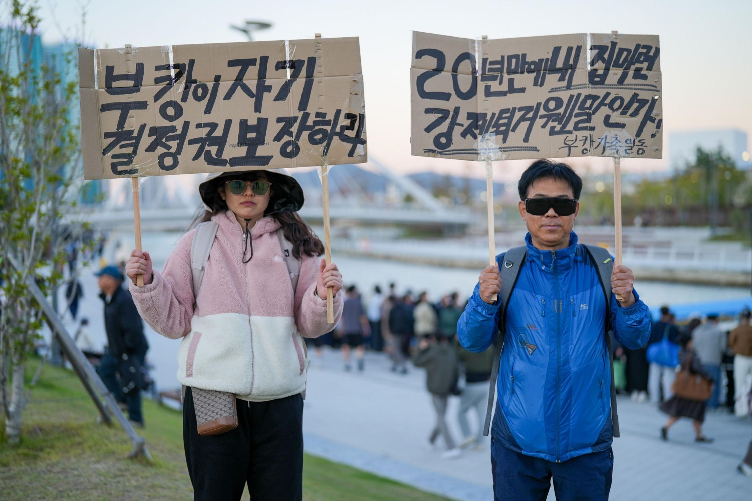Image caption,Jeong protesting against Bukangi's "eviction", alongside a man demanding officials "protect Bukangi's right to self-determination"