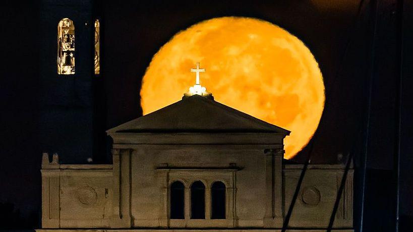 Image caption,The Moon can take on an orange or reddish hue when it is low in the sky due to the scattering of short wavelength blue light as it passes through a large depth of the atmosphere, as shown here as it rises behind the Basilica of the Madonna dei Martiri in Molfetta, Italy