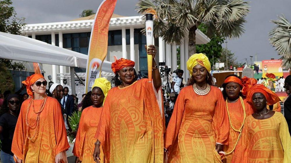 Image caption,IOC president Kirsty Coventry (left) joined a group of Senegalese women known as Lingueres to welcome the Olympic flame to Dakar in September