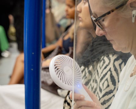 A traveller tries to keep cool with a handheld fan.Photograph: Linda Nylind/The Guardian