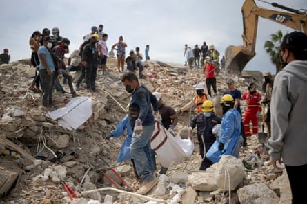 Volunteers remove a body from the wreckage of OPPE 27 while people watch.