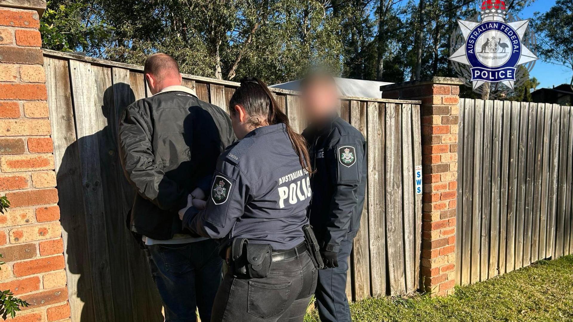 Image caption,A handout photo by police shows Hamish, who can only be seen from the back, being handcuffed by police