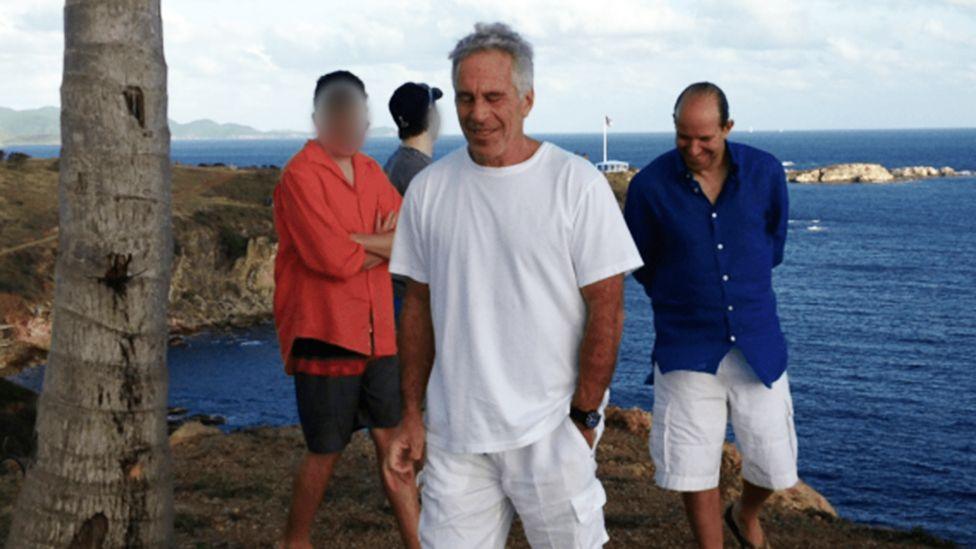 Image caption,A 2012 snapshot discovered in the Epstein files shows Lutnick (right) and Epstein (centre) on Little St James