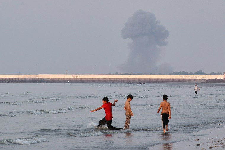 Three boys play in the shallow waters of the Strait of Hormuz, as a plume of smoke rises from an explosion off Bandar Abbas, Iran, on Monday.Razieh Poudat / ISNA via AP