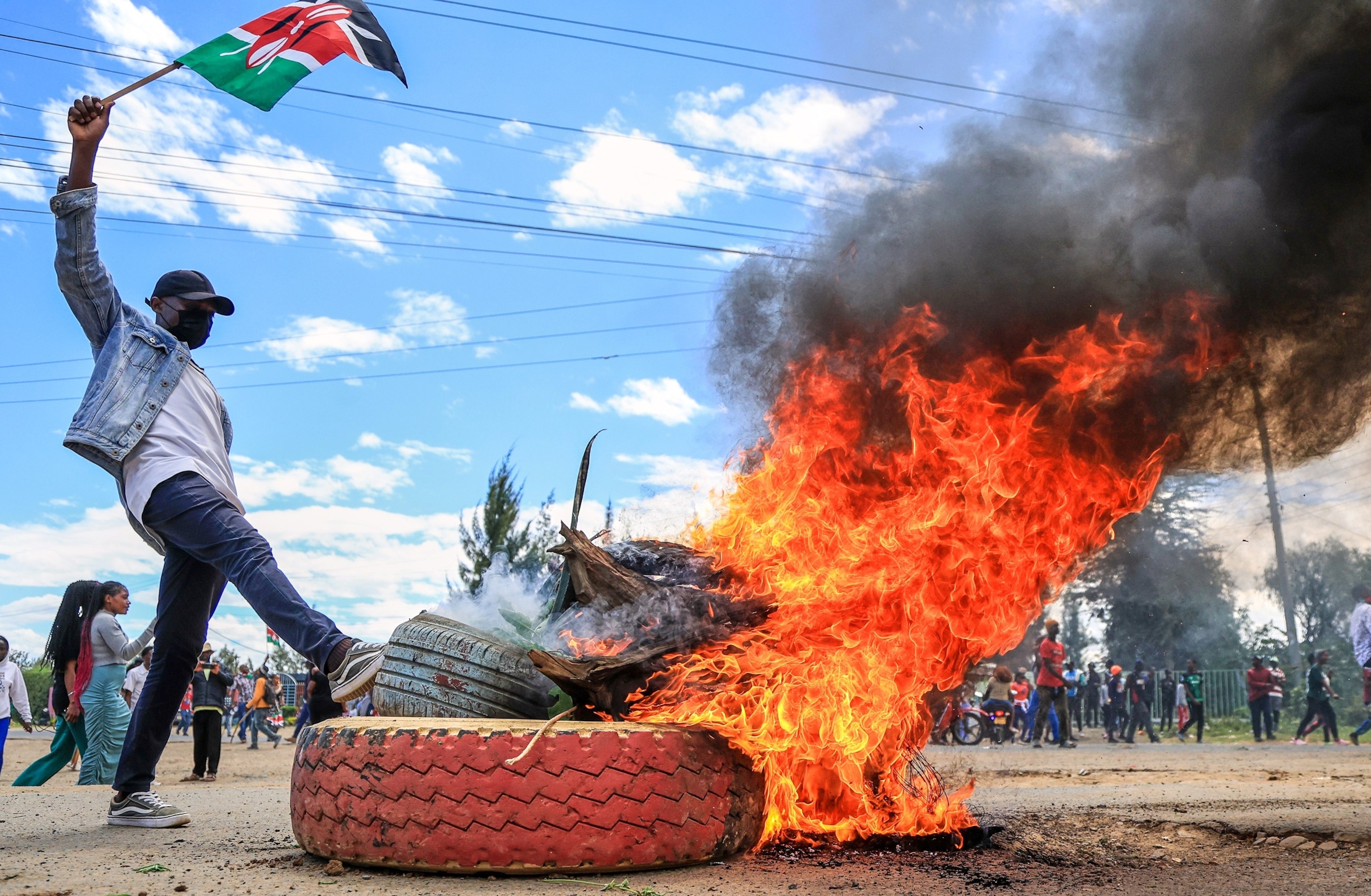 In this June 1, 2026, file photo, a protester raises a Kenyan flag near a burning barricade during a demonstration against a proposed Ebola quarantine center to be established by the United States at Laikipia Air Base in Nanyuki, Kenya.Andrew Kasuku/AP Photo, FILE