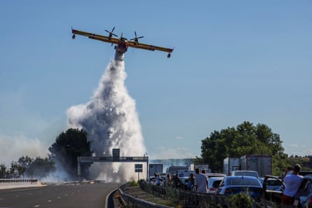 People watch as a firefighting plane tackles a wildfire next to the A9 motorway near Béziers, in south-west France.Photograph: Abdul Saboor/Reuters