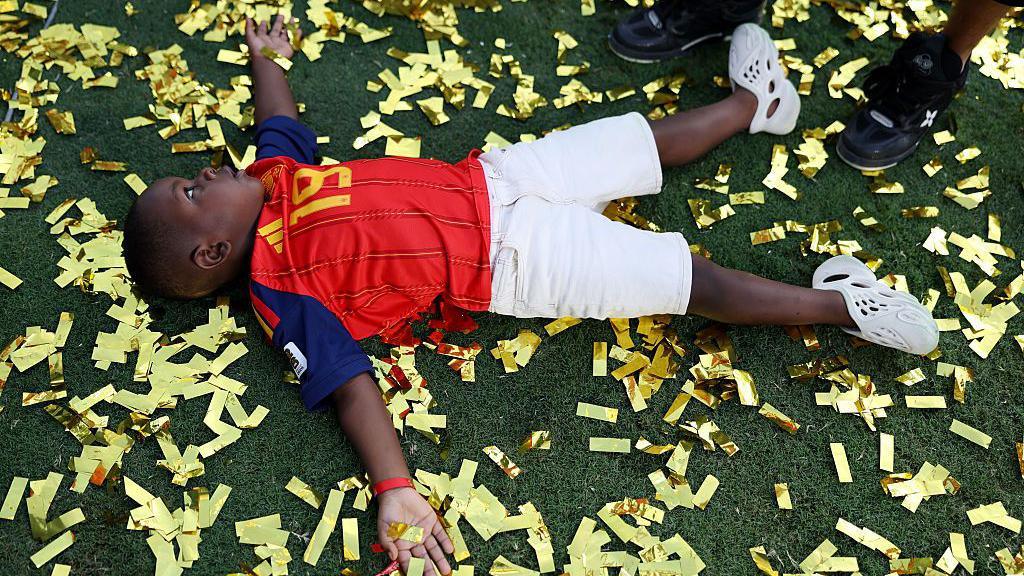 Image caption,Kenye lies on the ground surrounded by golden confetti
