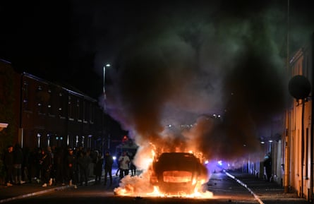 A vehicle burns as riot squad officers battle protesters throwing projectiles on 10 June in Ballymena, Northern Ireland.Photograph: Charles McQuillan/Getty Images