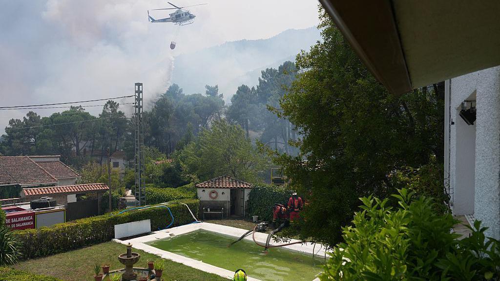 Image caption,A helicopter dumps water as firefighters collect water from a pool in El Tiemblo, outside Madrid