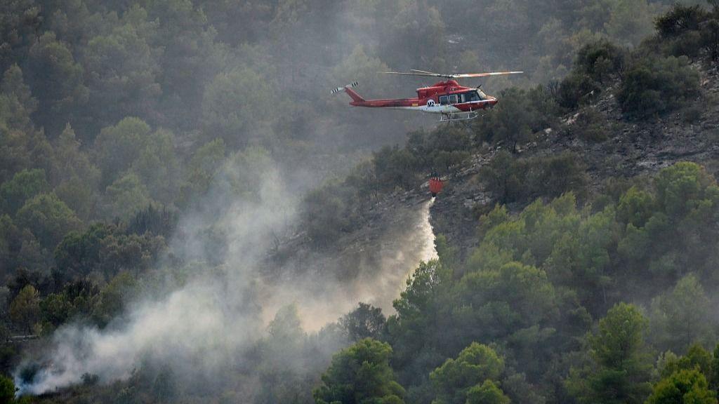 Image caption,A firefighting helicopter dumps water on a wildfire near Betxi, north of Valencia
