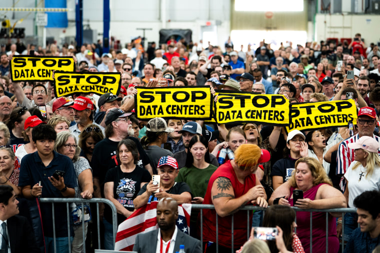 Demonstrators hold up "Stop Data Centers" signs as President Donald Trump speaks in Michigan on July 27.Sarah Rice / Bloomberg via Getty Images