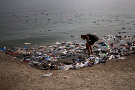 A man bends down to pick up a pair of shoes from debris washed up on Ceuta’s shore.Photograph: Pedro Nunes/Reuters