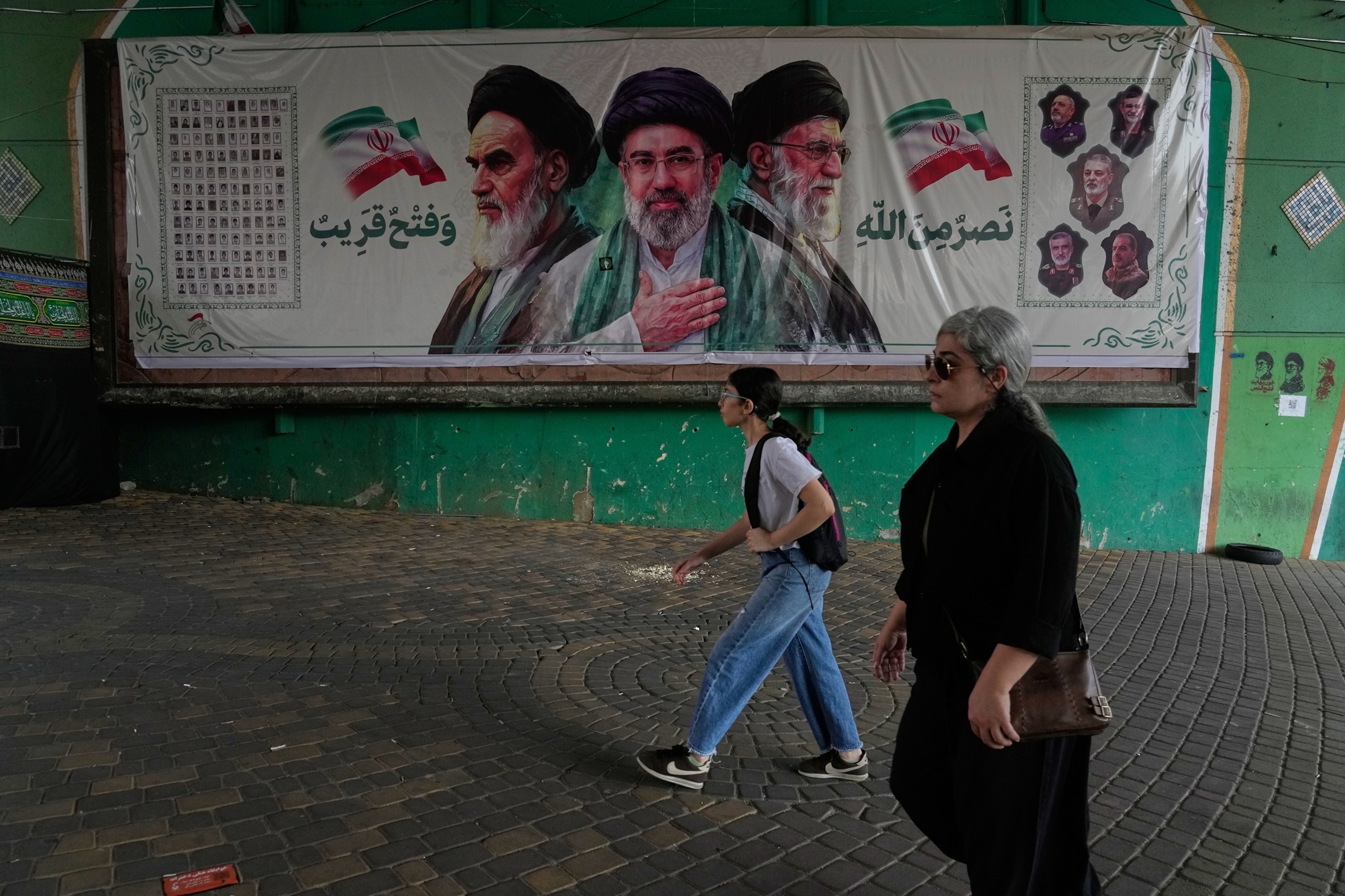 Women walk past a banner showing portraits of the late Iranian revolutionary founder Ayatollah Ruhollah Khomeini (L), Supreme Leader Ayatollah Mojtaba Khamenei (C), and the late Supreme Leader Ayatollah Ali Khamenei, under a bridge in northern Tehran, Iran, on Aug. 2, 2026.Vahid Salemi/AP Photo