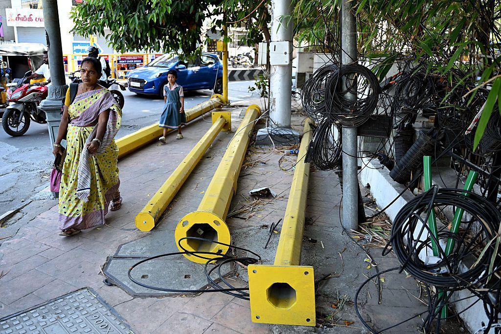 Image caption,A woman walks past poles and wires strewn across a footpath in Chennai