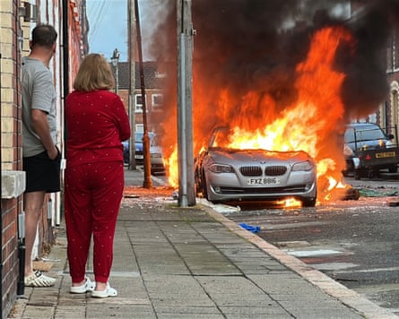 A couple stand outside a house as a vehicle burns on McMaster Street, in east Belfast.Photograph: PA