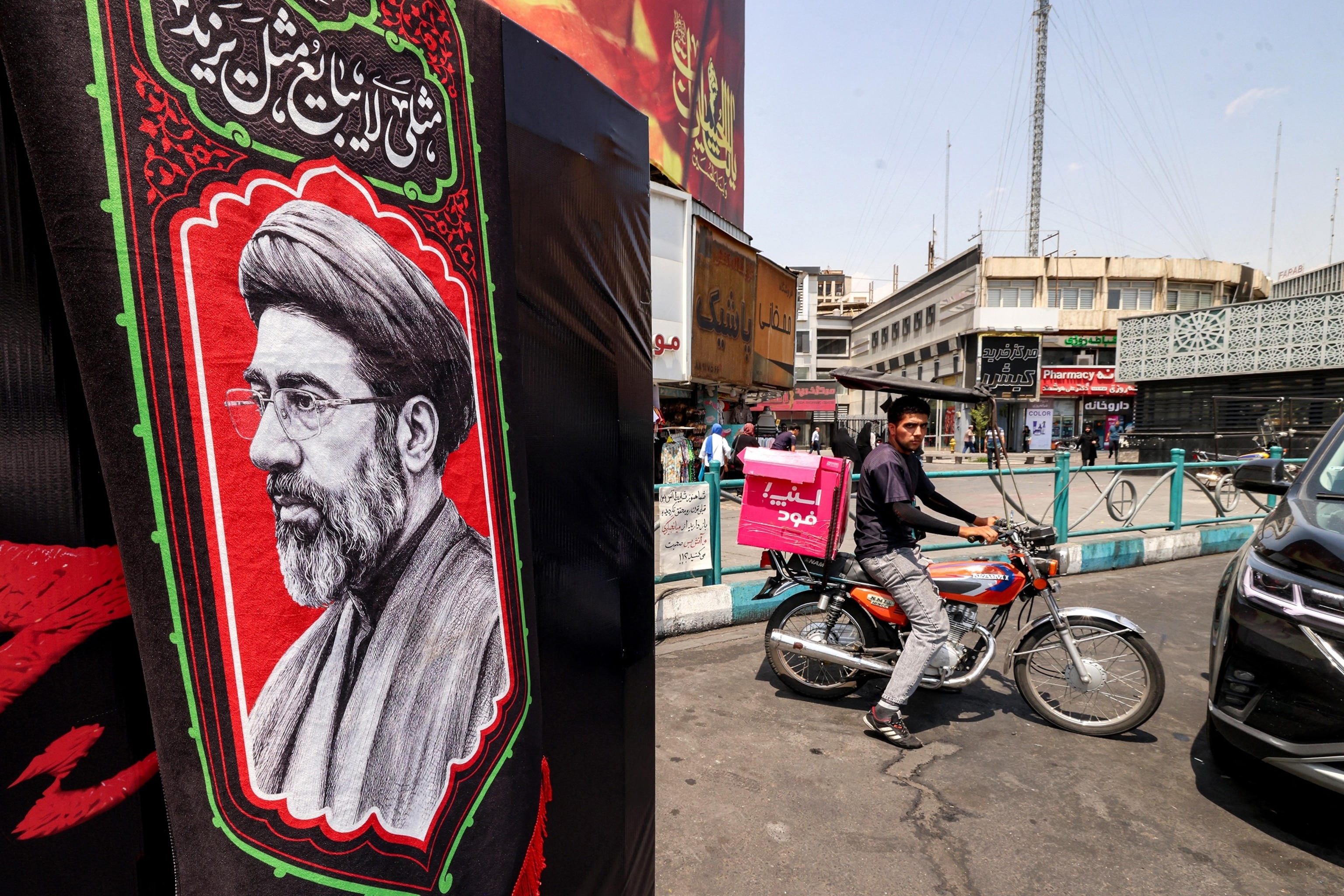 A delivery person rides a motorcycle near an image of Iran's Supreme Leader Mojtaba Khamenei at Valiasr Square in central Tehran on Aug. 8, 2026.Atta Kenare/AFP via Getty Images