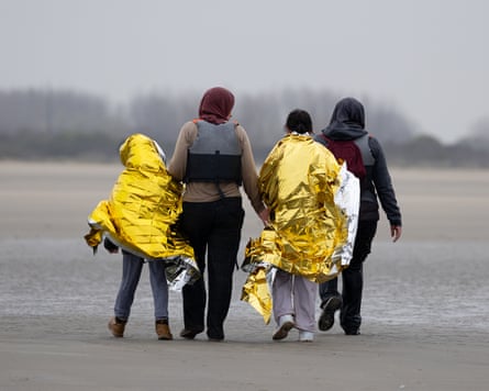 Two children in foil blankets and two women walk along the beach in Gravelines, France, after failing to board a dinghy attempting to sail into the Channel in April.Photograph: Tom Nicholson/Getty Images