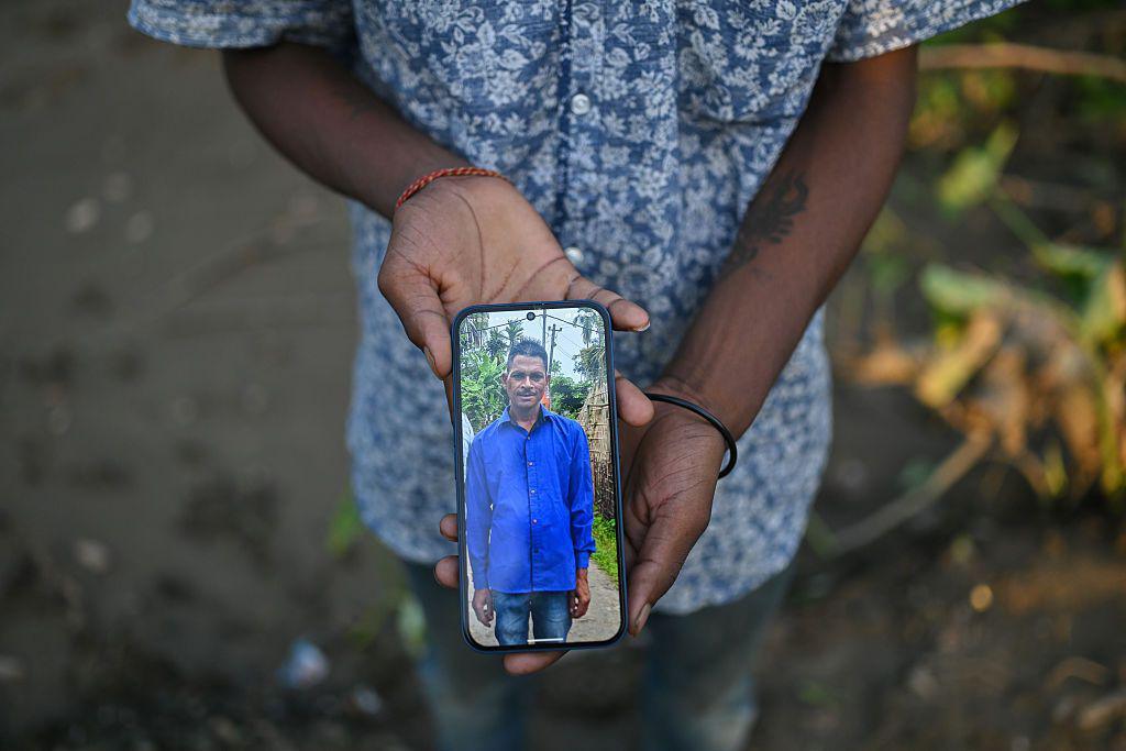 Image caption,Amit Giri holds a photo of his father, Siv Sankar Giri, who died in the floods, outside their damaged home in Sivasagar. He is among 100 people killed in the floods.