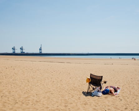 A woman sunbathing on a beach with the works in the distance.Photograph: Jon Pountney