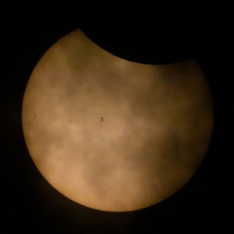 The sun during a partial solar eclipse and partially obscured by clouds, the International Space Station silhouetted as it transits at roughly five miles per second.Photograph: Nasa Handout/EPA