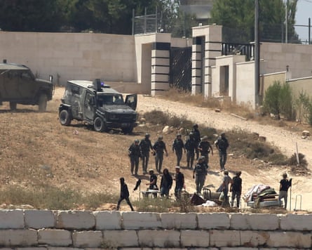 Israeli soldiers stand guard next to settlers in front of Palestinian homes that they have blockaded in the village of Qusra.Photograph: Nidal Eshtayeh/AP