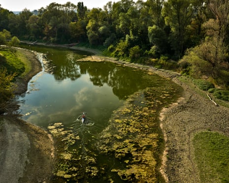 Tourists and passersby look down over the side of the Liberty bridge in Budapest. The remains of an older bridge can be seen the shallow waters below.