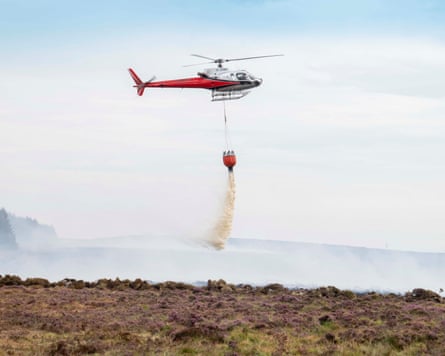A helicopter drops water over the land.Photograph: Adrian Sherratt/The Guardian