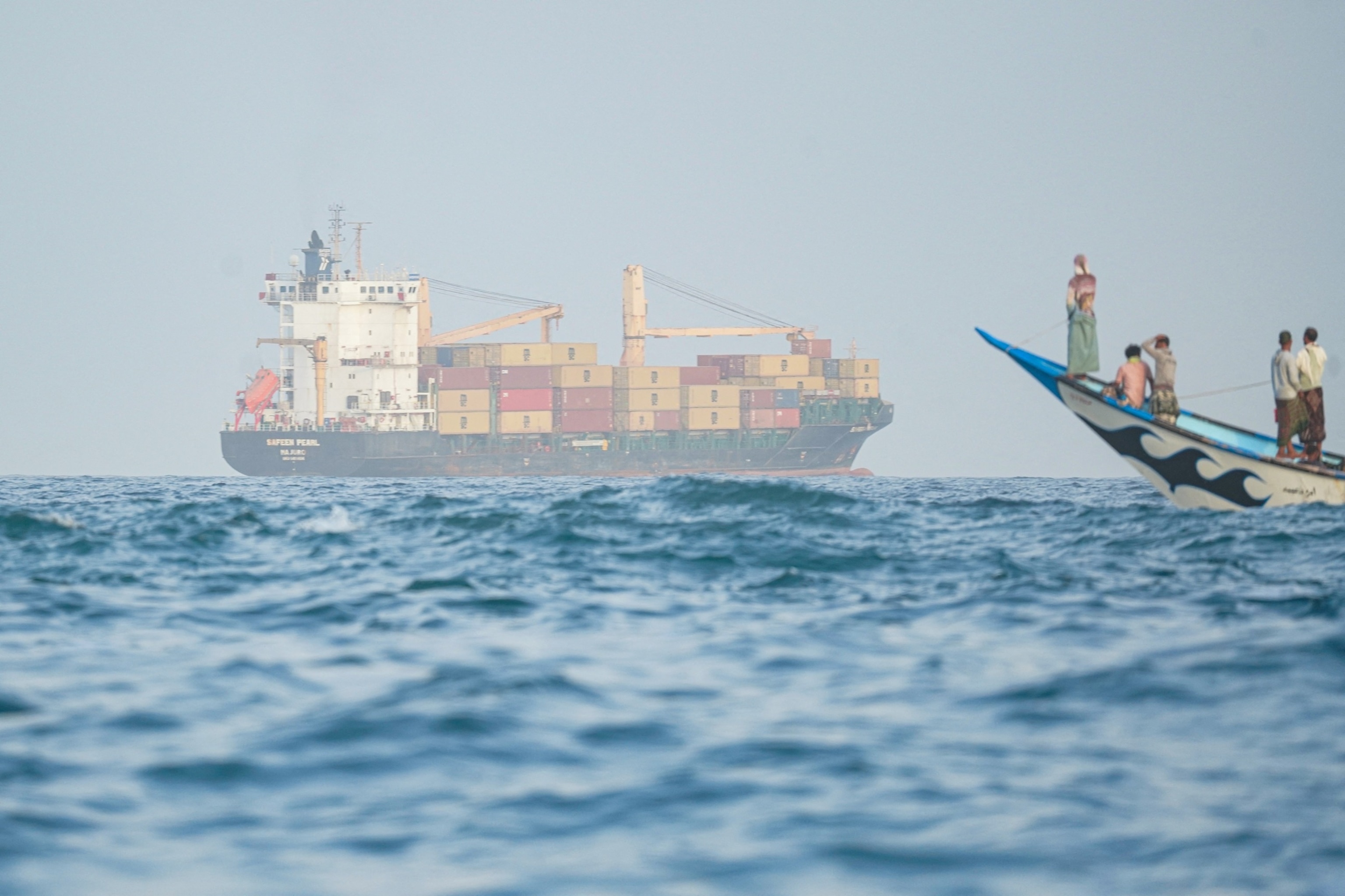 People sail their boat past container ships anchoring near the Strait of Bab al-Mandeb off Yemen's coast in the Gulf of Aden, August 6, 2026.AFP via Getty Images