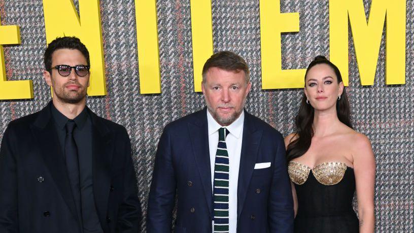 Image caption,Guy Ritchie (centre) with Theo James and Kaya Scodelario at a London launch for a previous series of The Gentlemen in 2024
