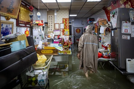A resident wearing a raincoat wades through flood water inside an inundated home in Zihguan District, Kaohsiung, Taiwan.Photograph: Cheng-Chia Huang/ZUMA Press Wire/Shutterstock