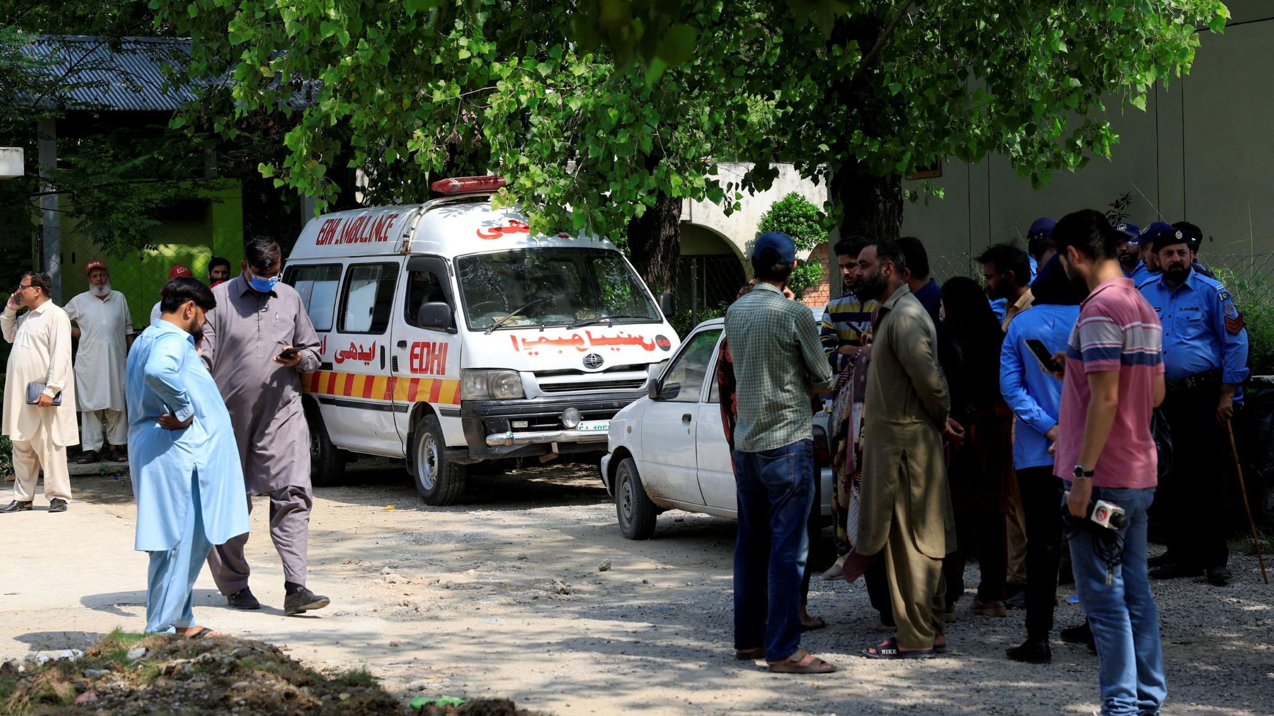 Image caption,Family members and police officers stand outside a mortuary following the deadly fire at the PIMS hospital