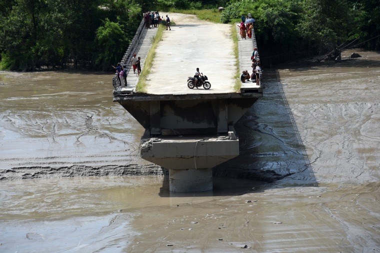 A local resident rides a motorcycle on the remains of a bridge swept away by floodwaters in Nuwakot, Nepal, on Wednesday.Sunil Pradhan / Anadolu via Getty Images