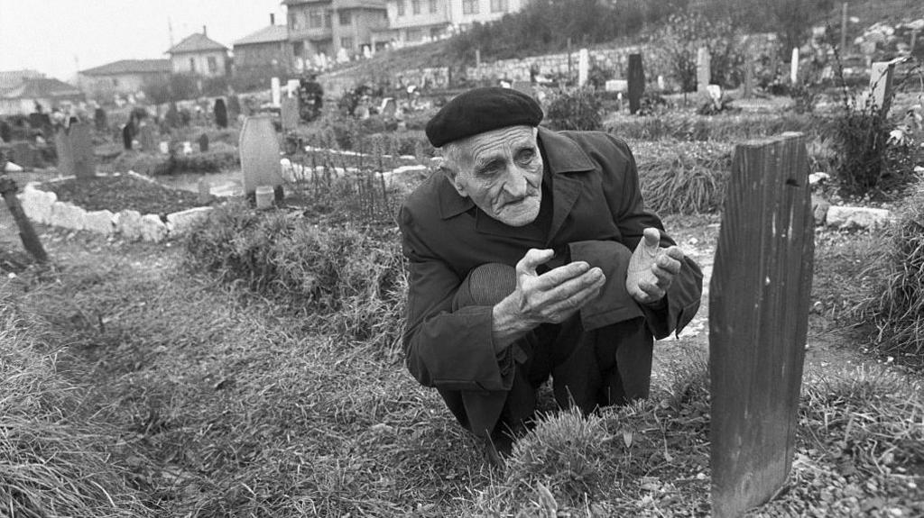 Image caption,A father kneels at his son's grave in Sarajevo