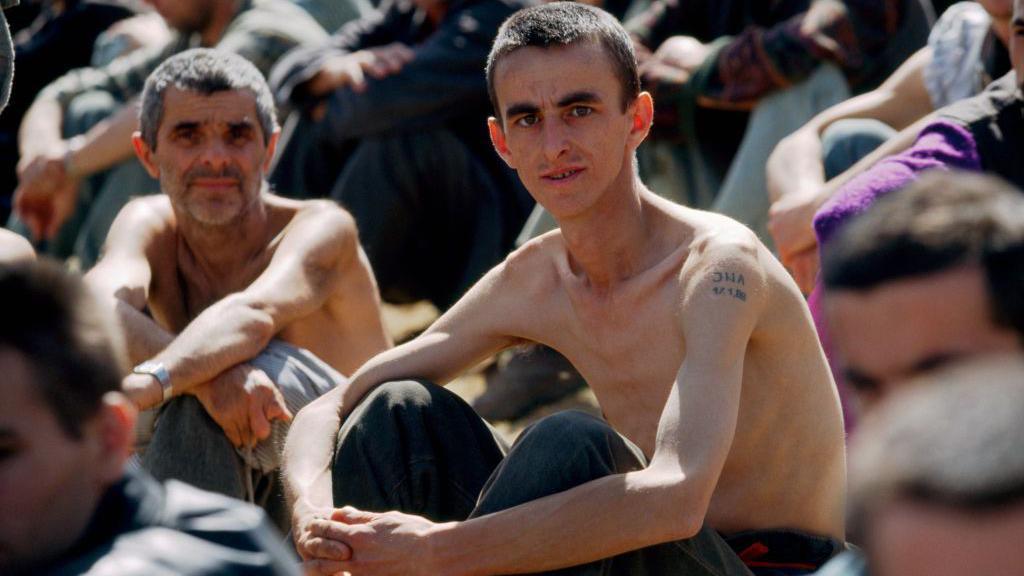 Image caption,Emaciated prisoners at a Bosnian Serb camp in 1992. Later, some of the survivors would attend the trial of Ratko Mladić