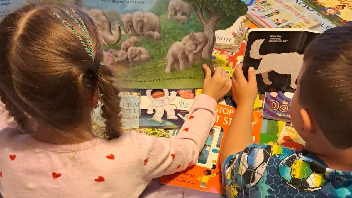 Image caption,In Dublin, Ireland, Helen Cashell's two children read books atop a pile of other titles they received in the post through Parton's Imagination Library