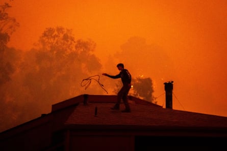 Sage Harvey tosses a rope off the roof of his house as the Plaskett fire approaches on Friday in Big Sur, California.Photograph: Ethan Swope/AP