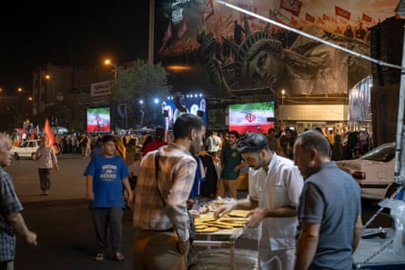 People buy bread from a street vendor beneath an anti-US billboard in Tehran.Photograph: Morteza Nikoubazl/NurPhoto/Shutterstock