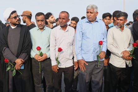 Men hold red roses as they attend a mass funeral  in Kuhestak.Photograph: Razieh Poudat/AP