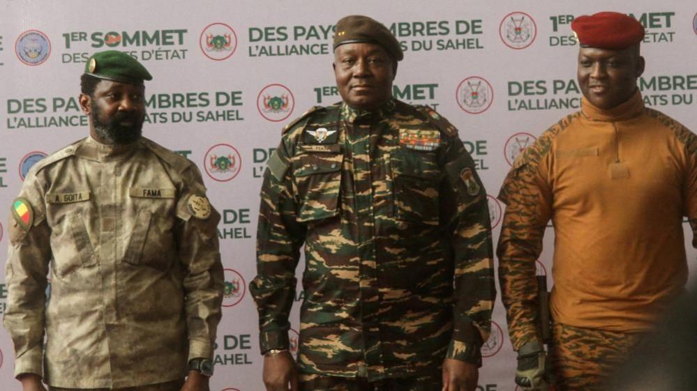Image caption,Niger's Gen Abdourahamane Tiani (C), Mali's Gen Assimi Goïta (L) and Burkina Faso's Capt Ibrahim Traoré (R) came together for the first heads of state summit of the AES in 2024