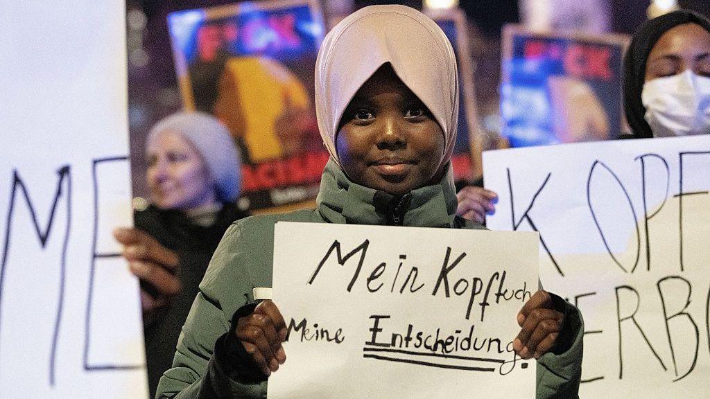 Image caption,An 11-year-old student protests the ban in Vienna back in February with the banner "meine Kopftuch, meine Entscheidung" - "my headscarf, my decision"